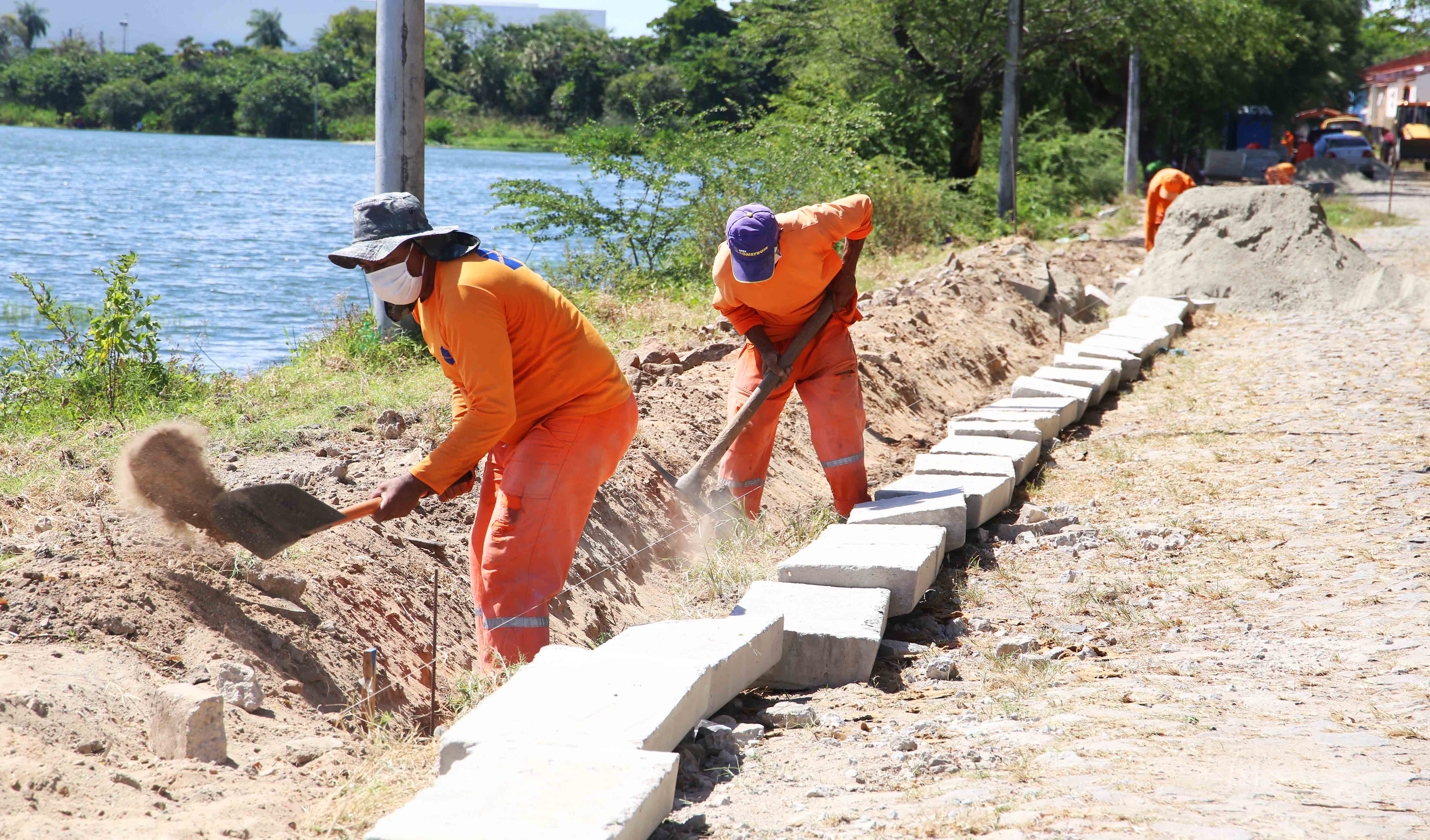 três operários trabalhando em meio-fio às margens da Lagoa do Mondubim